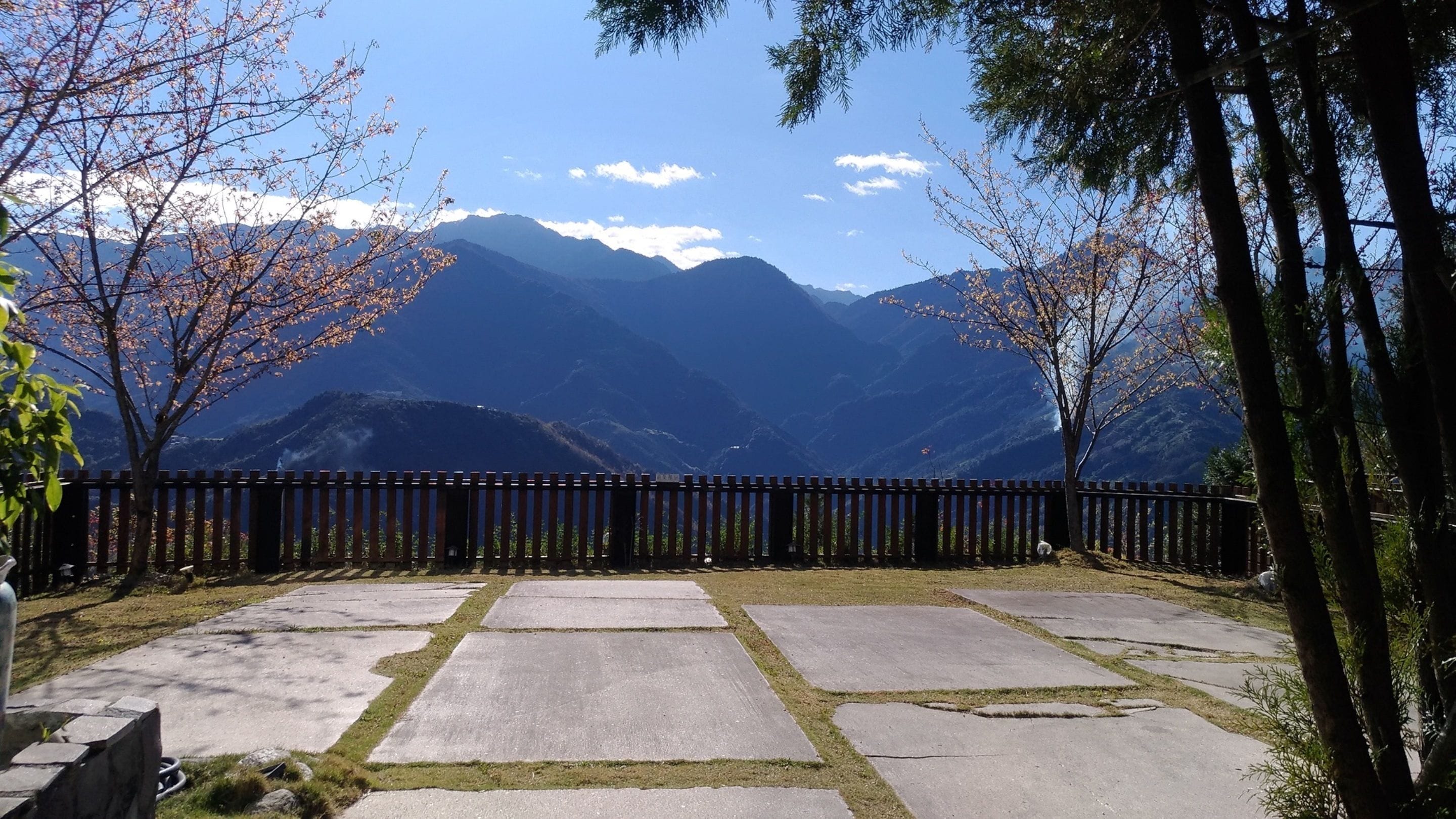 Un sentiero lastricato che conduce a una vista sulle montagne, con una recinzione in legno e alberi.