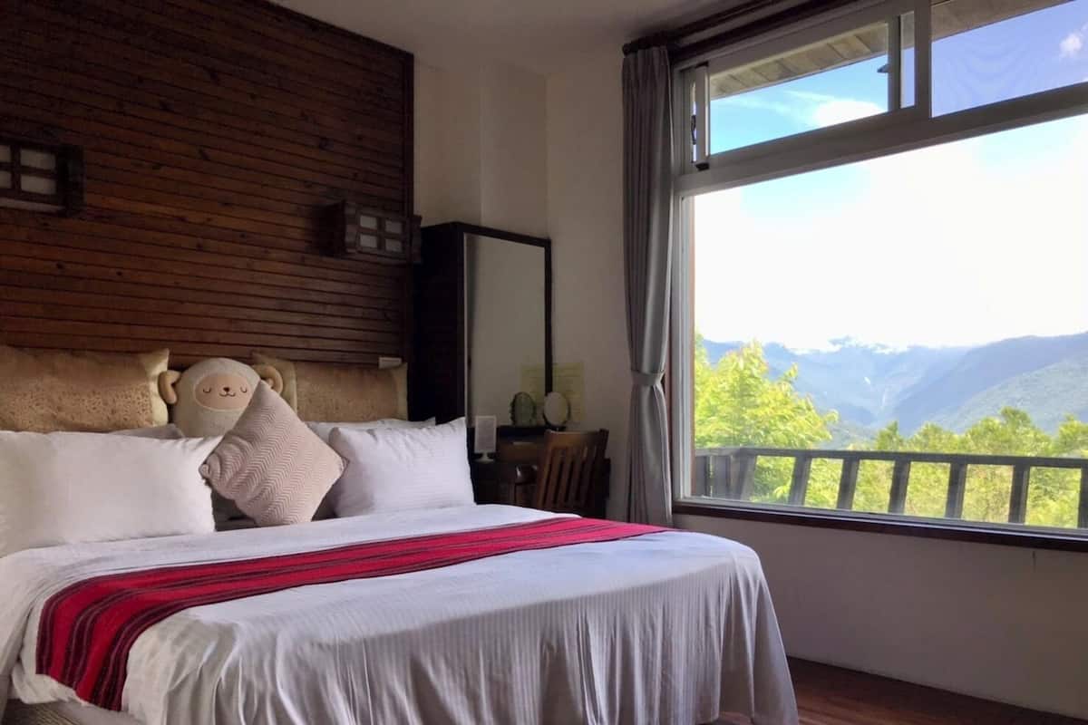 A bedroom with a large bed, wooden headboard, and a view of mountains through a window.