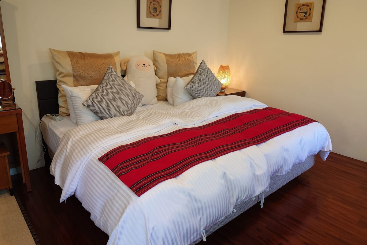 A neatly made bed with a red and white striped blanket, multiple pillows, and a bedside lamp.