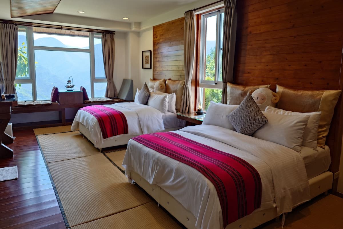 A hotel room with two beds, a wooden wall, large windows, and a view of the mountains.