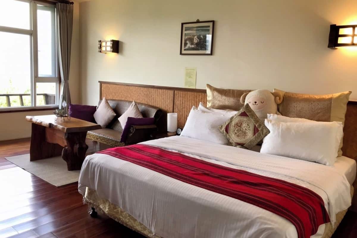 A hotel room with a large bed, a wooden nightstand, a lamp, and a window with curtains.