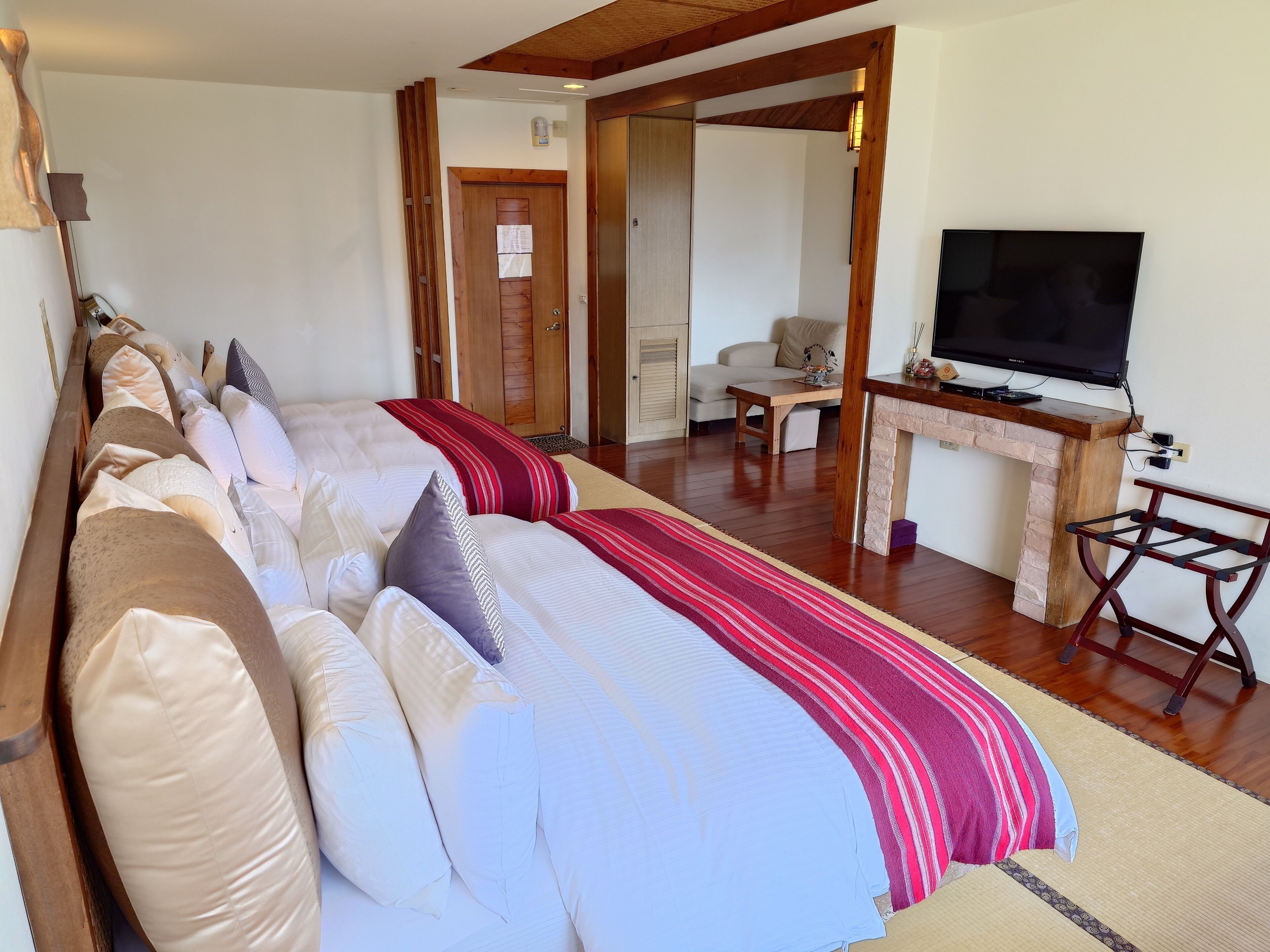 A spacious bedroom with a large bed, a wooden desk, a television, and a seating area with a sofa and armchair.