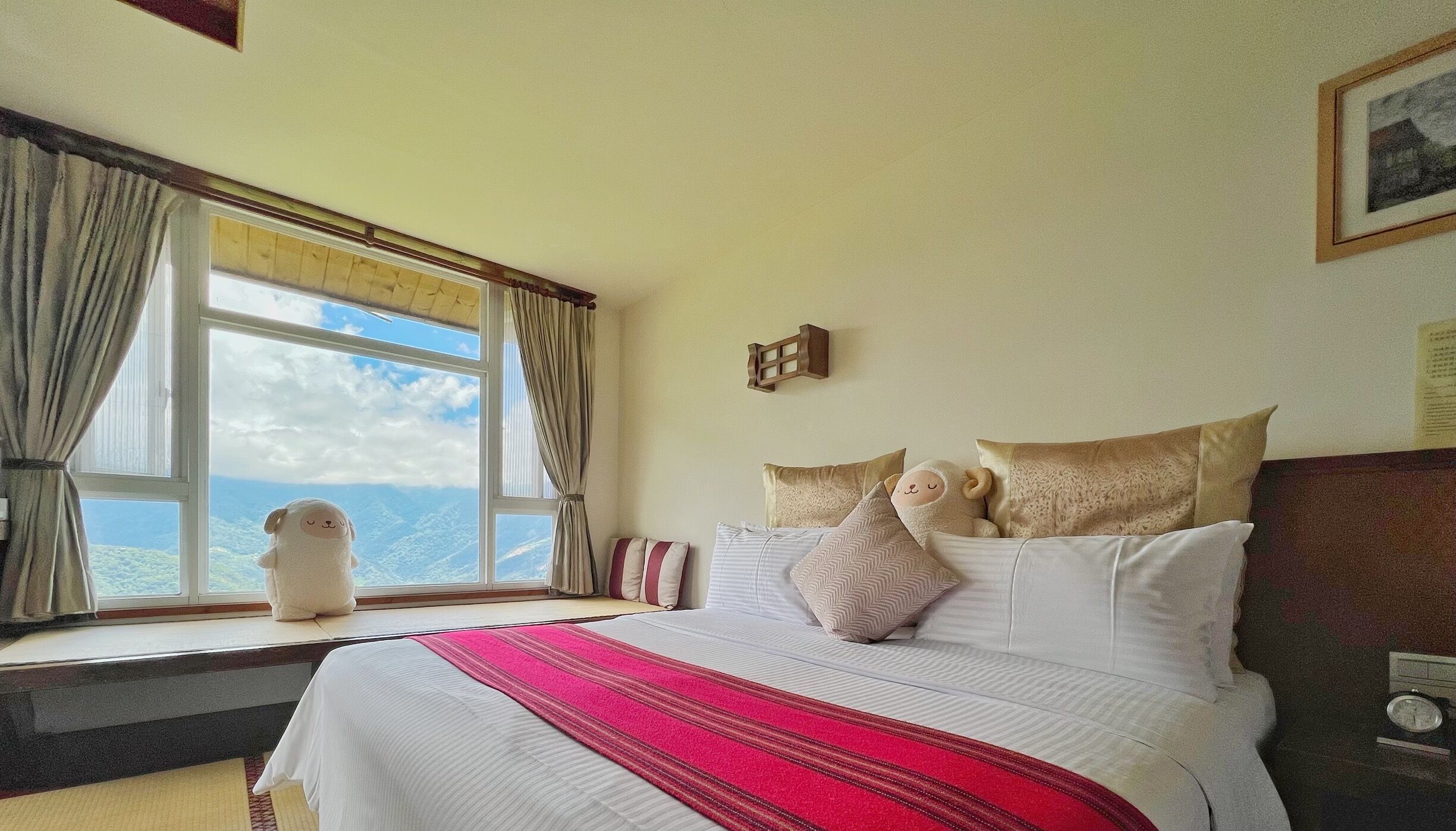 Ein Hotelzimmer mit einem großen Bett, einem Fenster mit Vorhängen, Blick auf die Berge und einer kleinen Holzeinrichtung mit einem dekorativen Gegenstand.