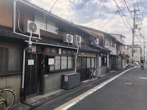 A narrow street with traditional Japanese buildings, air conditioning units, and bicycles.
