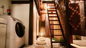 A laundry room with a washing machine, a wooden ladder, and a stone pathway leading to a bamboo fence. - Kyoto Traditional Machiya House (Kyoto)
