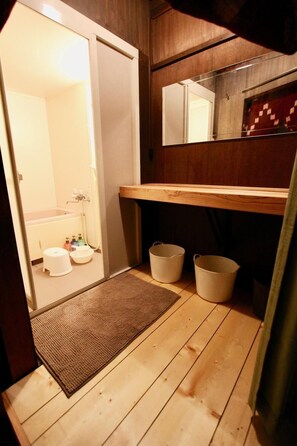 A small bathroom with a wooden floor, a white sink, two white buckets, and a mirror above the sink.