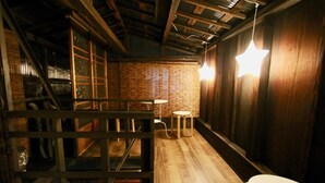 A dimly lit room with wooden floors, a brick wall, and a metal staircase. There are two round tables and a chair. - Kyoto Traditional Machiya House (Kyoto)