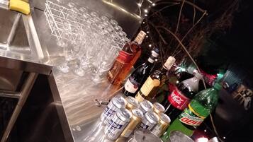 A bar area with a stainless steel counter, glasses, bottles, and cans.