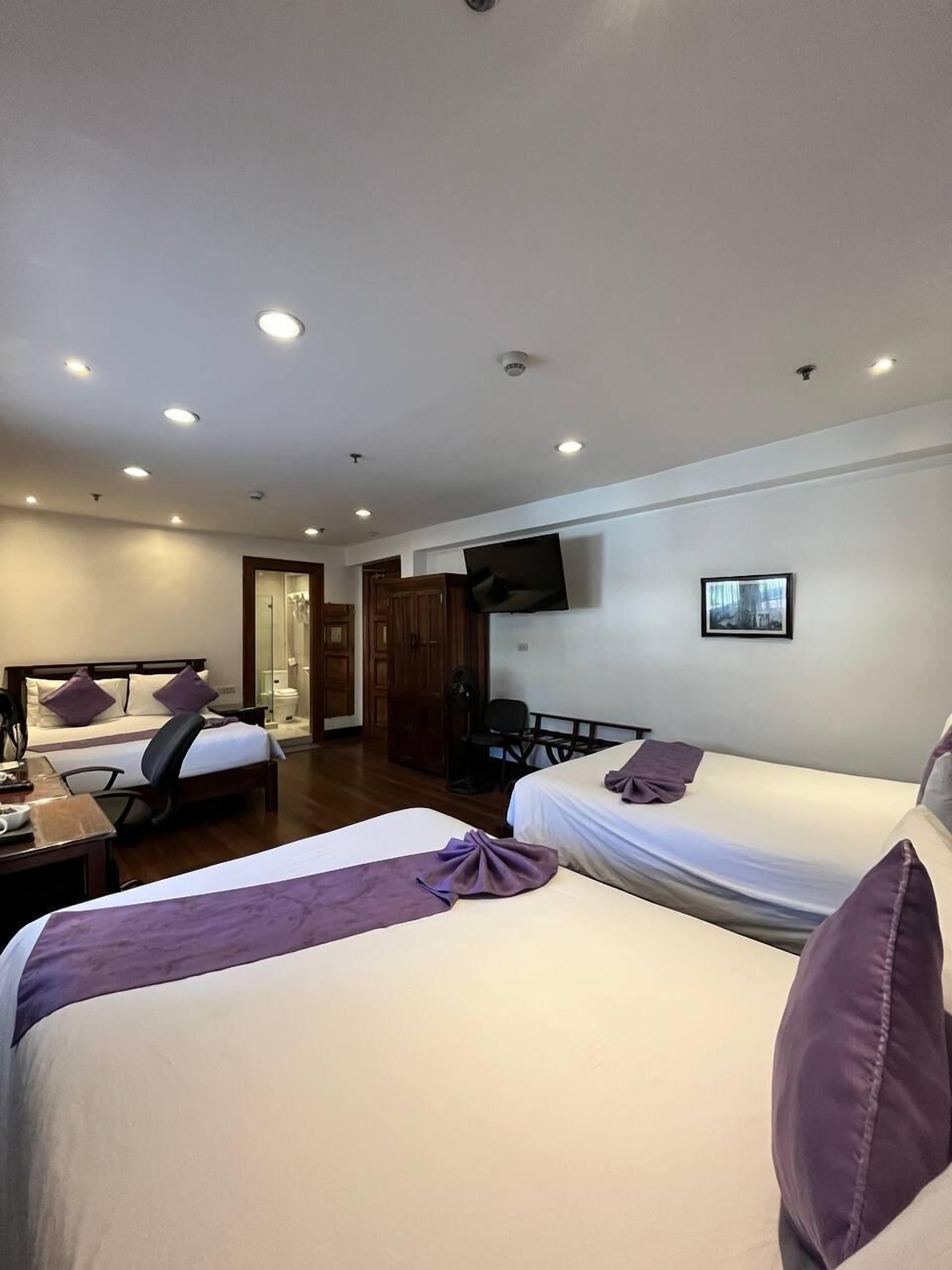 A hotel room with two beds, a desk, a chair, a TV, and a bathroom visible through an open door.