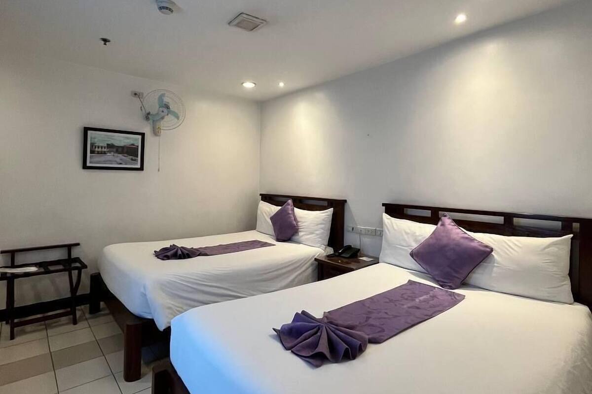 A hotel room with two beds, a desk, and a fan.