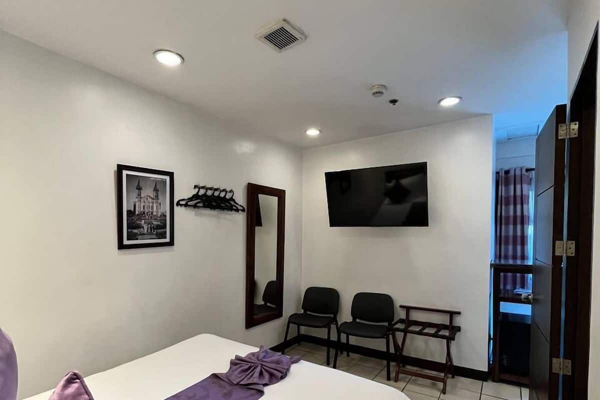 A hotel room with a bed, a TV mounted on the wall, a coat rack, and a door leading to a bathroom.
