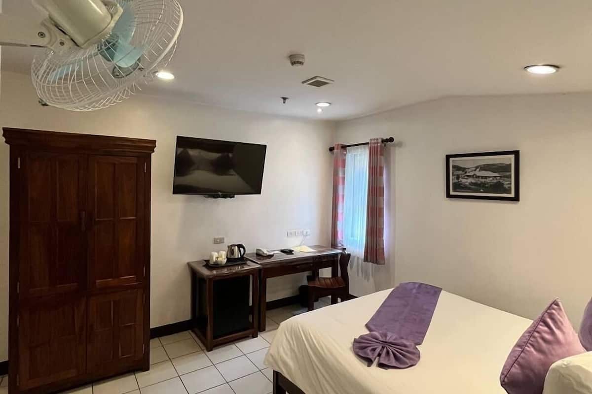 A hotel room with a bed, a desk, a TV, a wardrobe, and a ceiling fan.