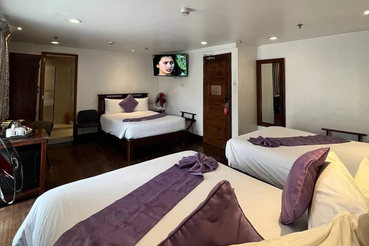 A hotel room with two beds, a TV mounted on the wall, a desk with a chair, and a door leading to another room.