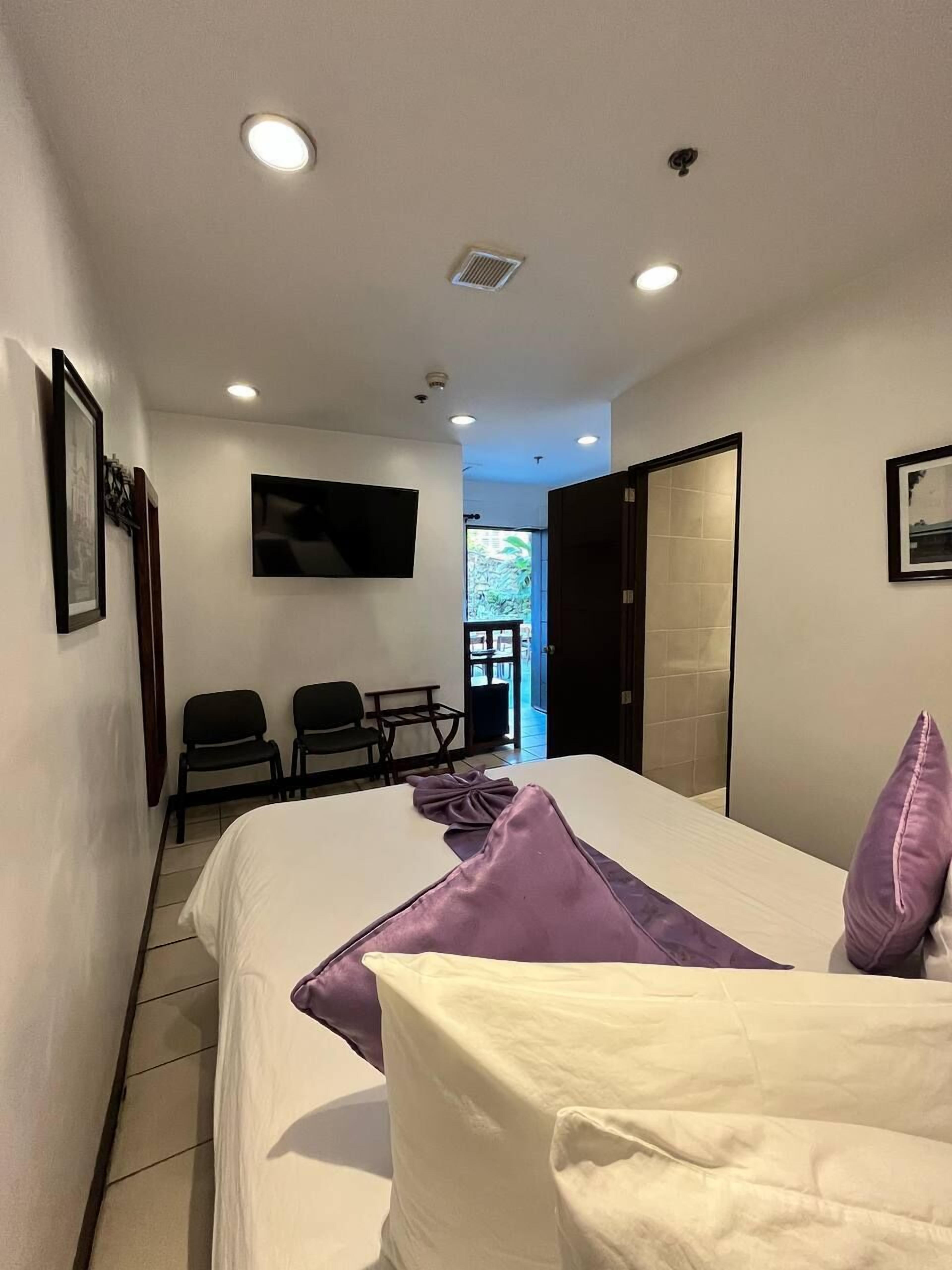 Une chambre d’hôtel équipée d’un lit, d’un téléviseur fixé au mur et d’un coin salon avec des fauteuils.