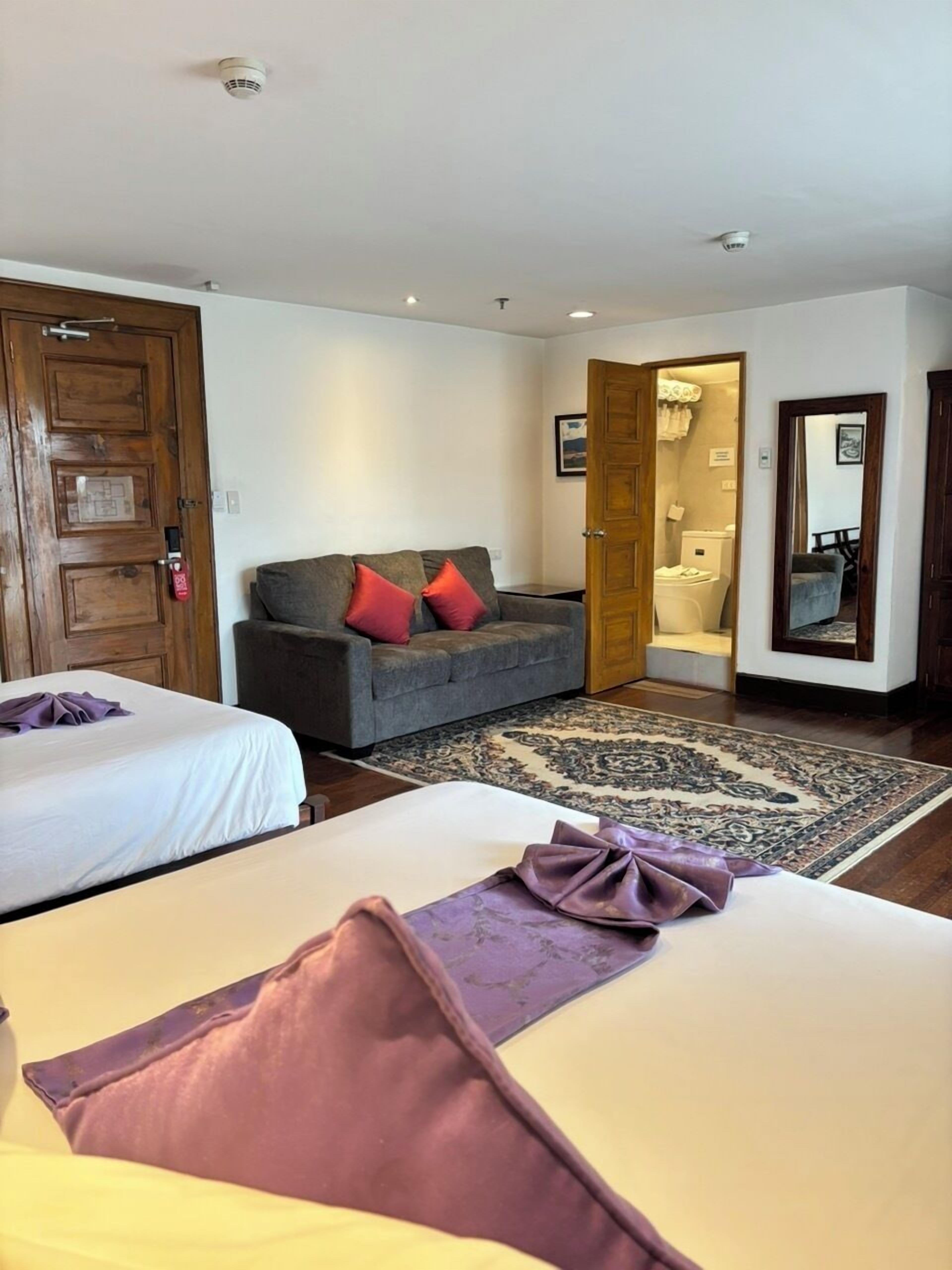 A hotel room with two beds, a sofa, and a bathroom visible through an open door.