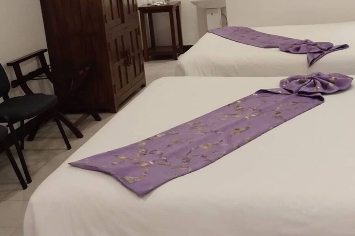 A hotel room with two beds, a wooden wardrobe, a desk, and two chairs.