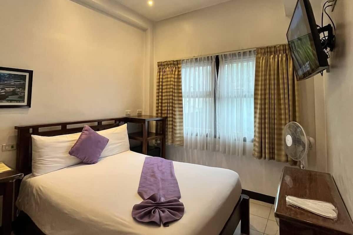 A hotel room with a bed, a desk, a TV, and a window with curtains.