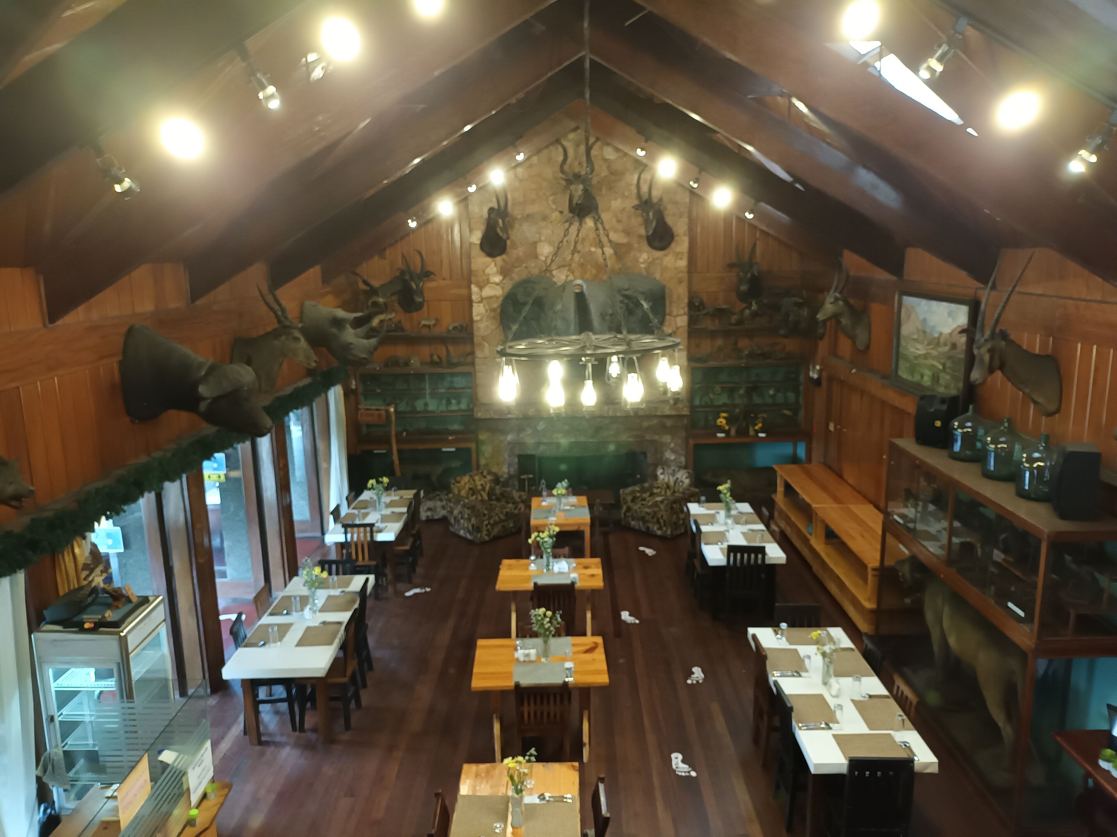 Un restaurante con paredes de madera, una chimenea de piedra y cuernos de ciervo colgados. Las mesas están dispuestas con manteles blancos y centros de mesa.