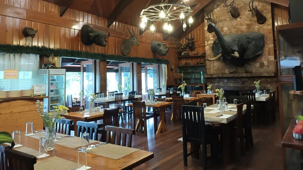 A restaurant interior with wooden walls, a stone fireplace, and various animal heads mounted on the walls. Tables are set with flowers and tableware. - Log Cabin Hotel-Baguio (Baguio)