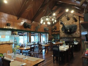 Interno di un ristorante con pareti in legno, un camino in pietra e diverse teste di animali appese alle pareti. I tavoli sono apparecchiati con fiori e stoviglie.