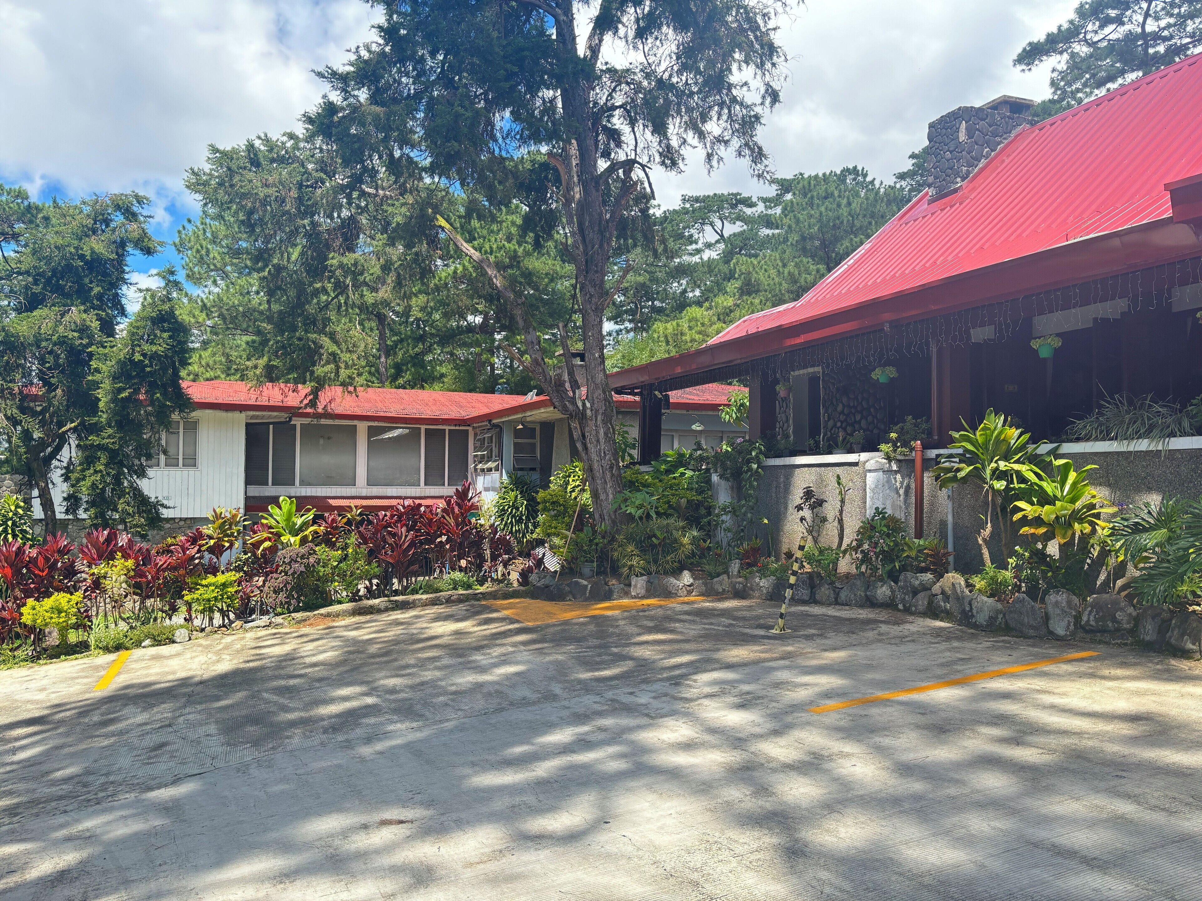 A building with a red roof and a stone wall. There are trees and plants around the building.