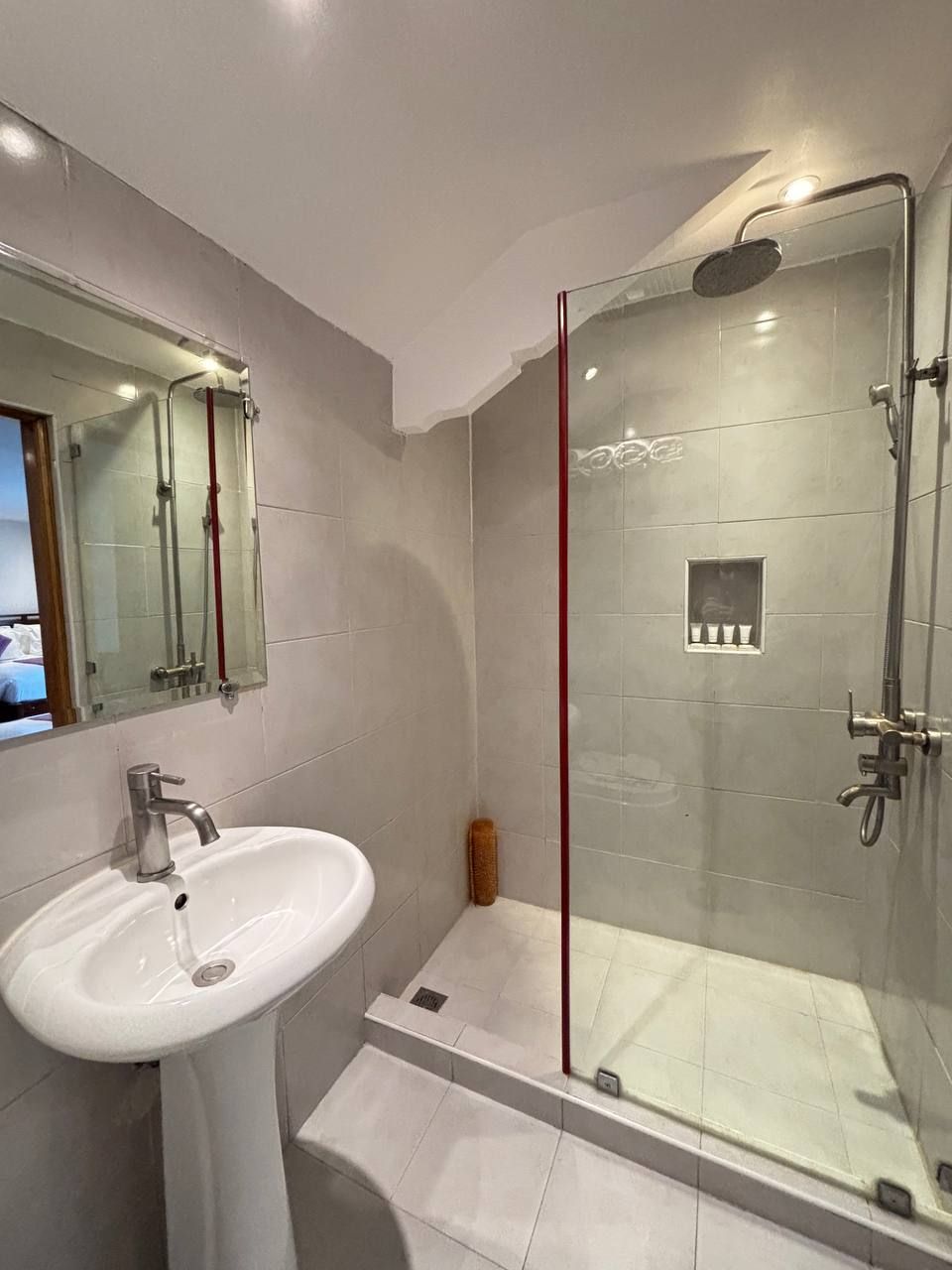 A modern bathroom with a glass-enclosed shower, a white sink, and a mirror above the sink.