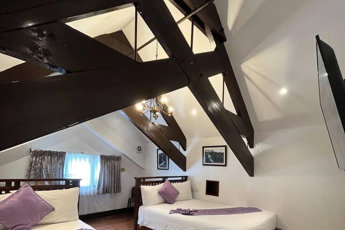 A bedroom with two beds, wooden beams, and a sloped ceiling.