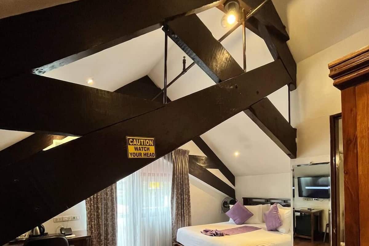 A bedroom with a sloped ceiling, a bed, a desk, and a television.
