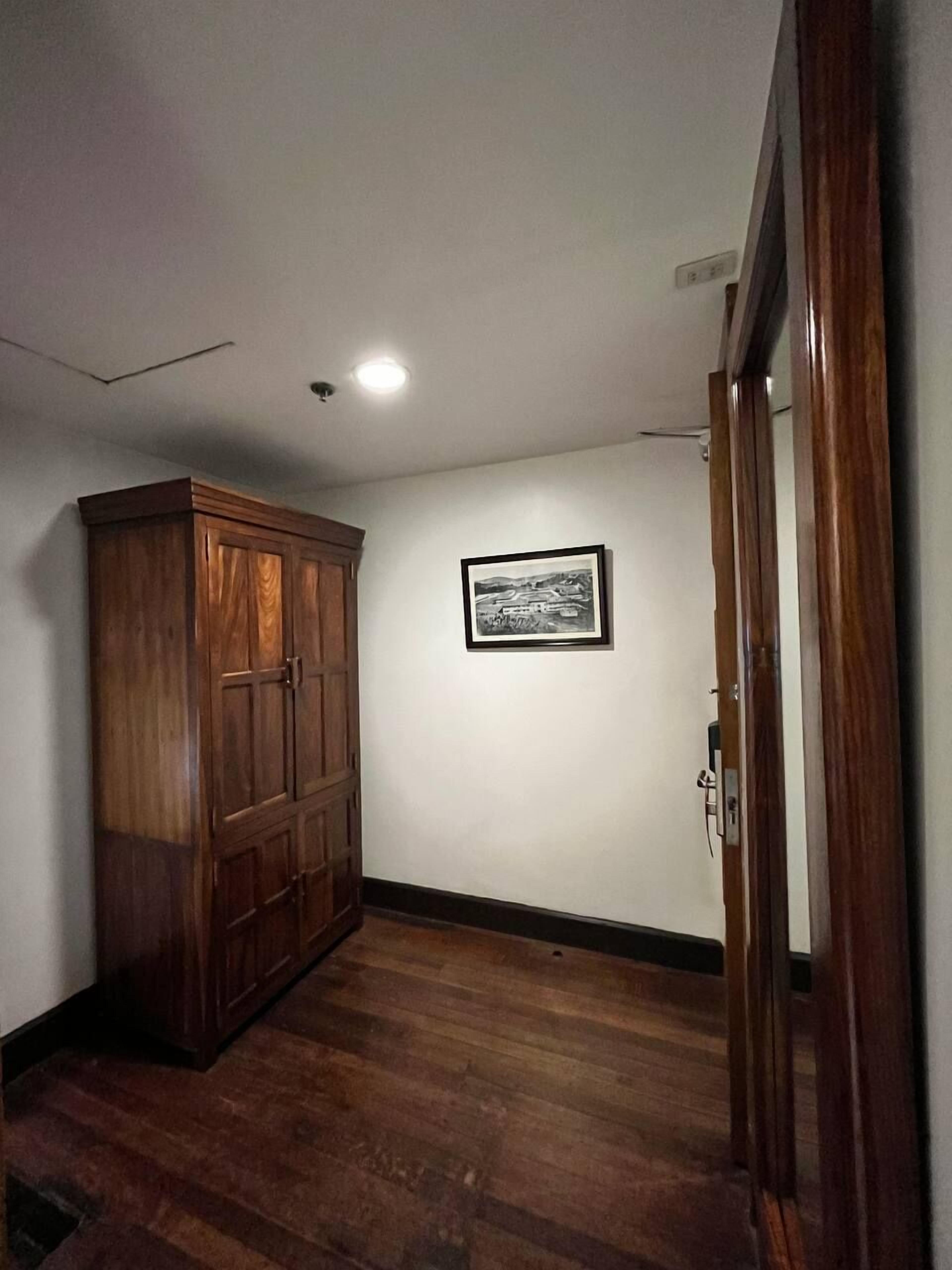 A hallway with wooden flooring, a wooden wardrobe, a framed picture on the wall, and a door on the right.