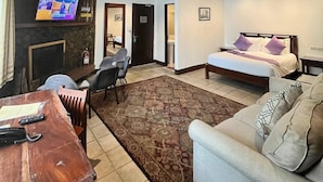 A hotel room with a wooden ceiling, a bed with pillows, a sofa, a TV on the wall, and a desk with a telephone. - Log Cabin Hotel-Baguio (Baguio)