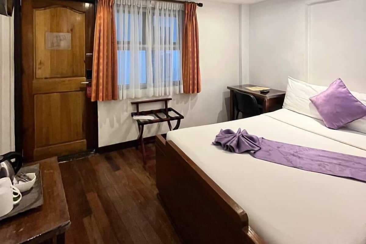 A hotel room with a bed, a desk, a chair, a wooden wardrobe, and a window with curtains.