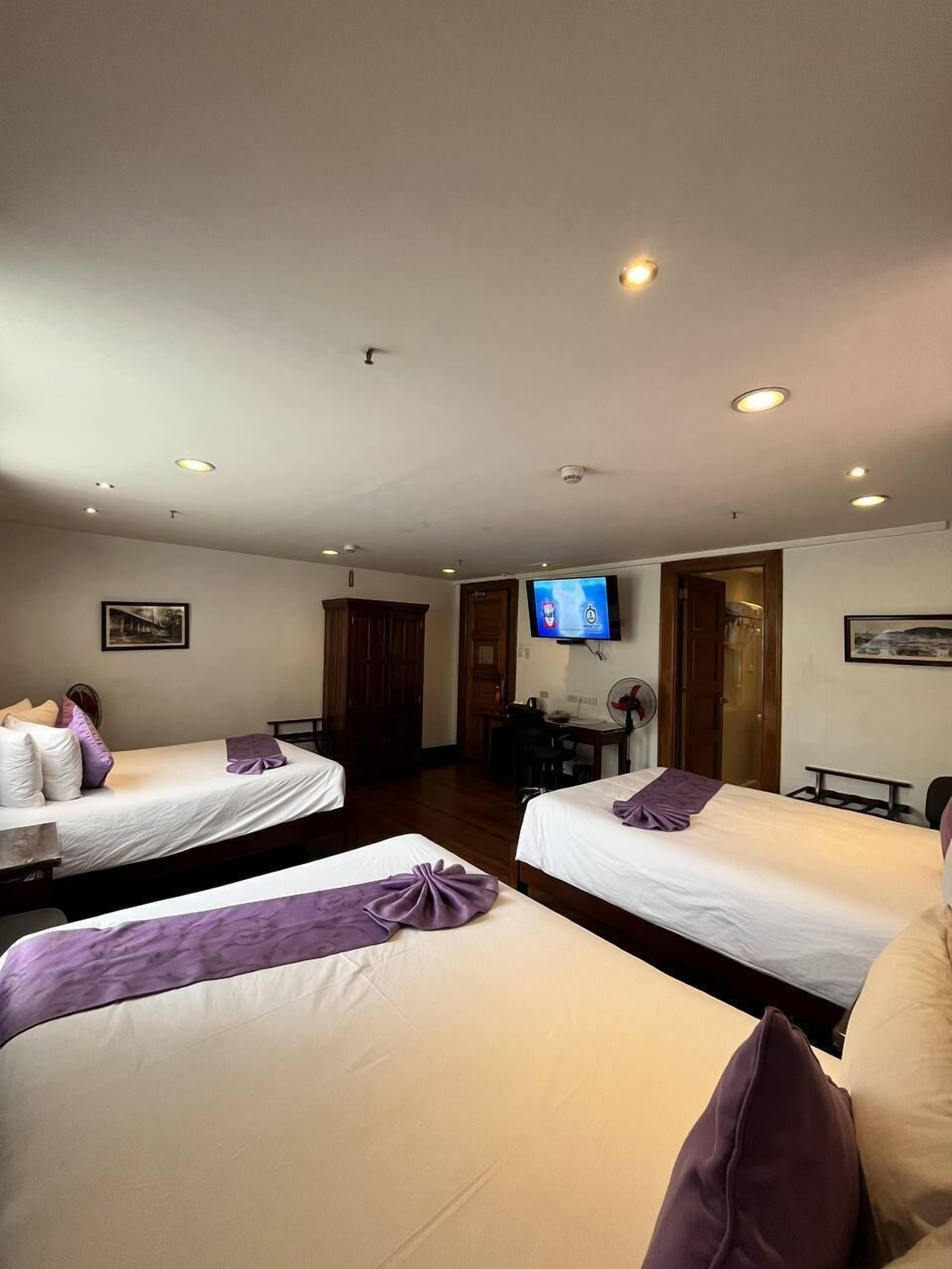 A hotel room with two single beds, a desk, a chair, a television, and a door leading to another room.
