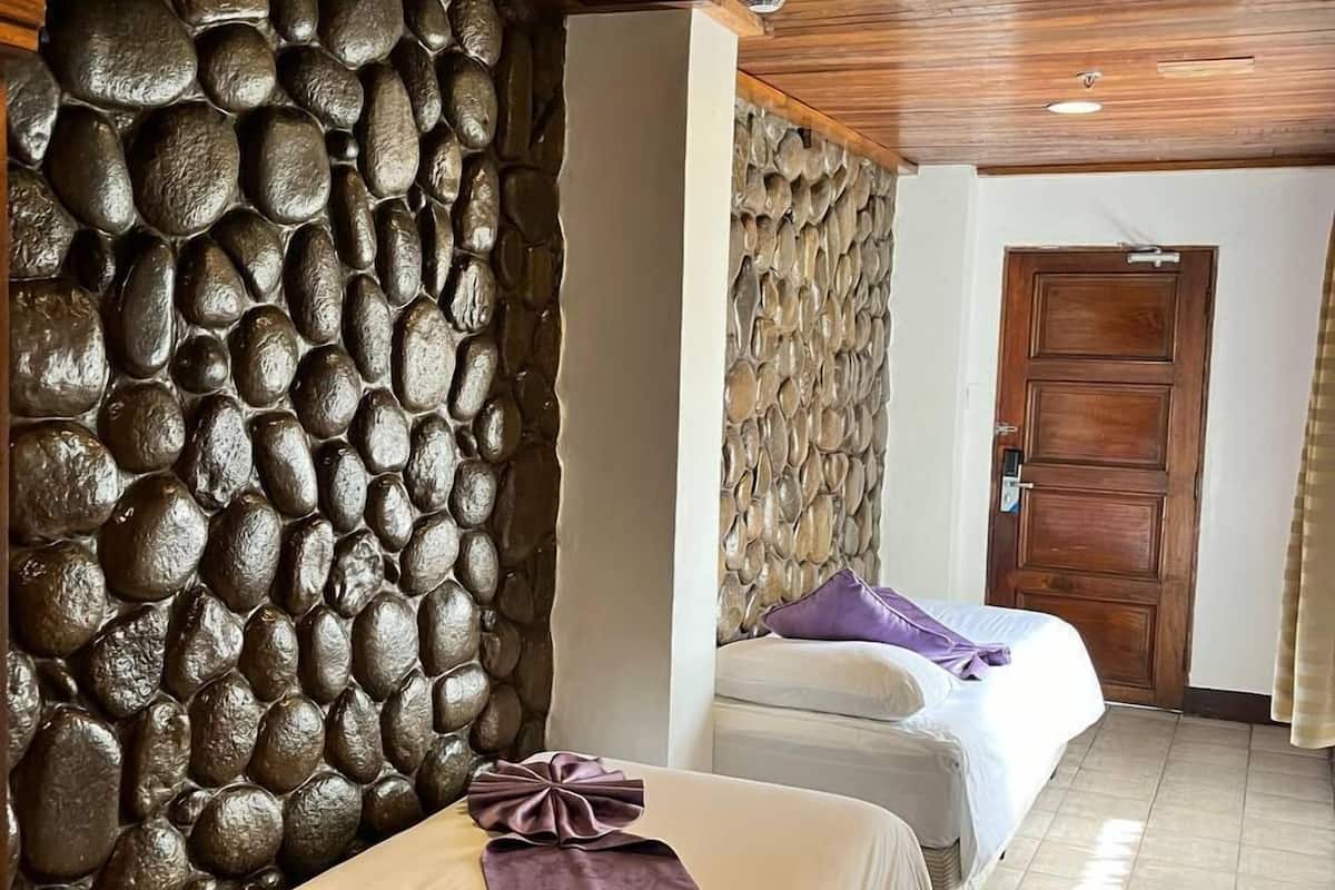 A hotel room with two beds, a stone wall, wooden ceiling, and a door.