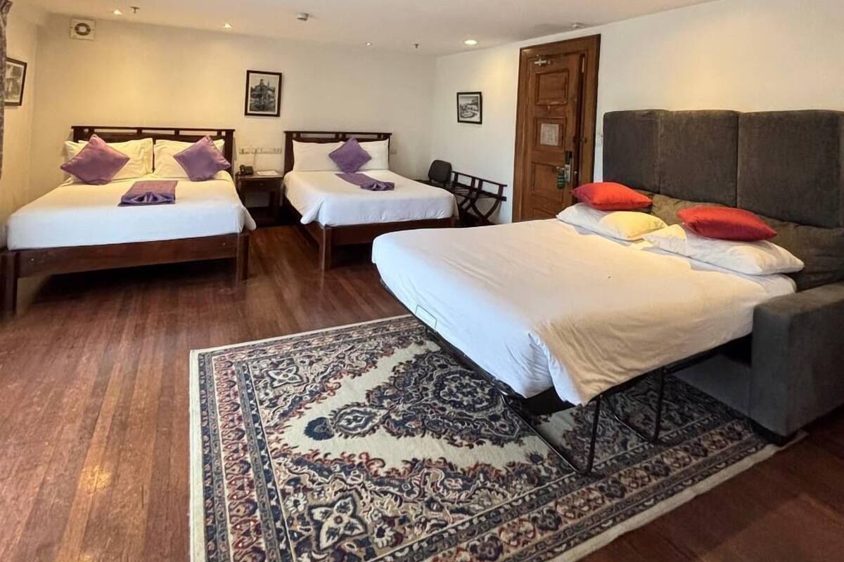 A hotel room with two single beds, a sofa bed, a patterned rug, and a wooden floor.