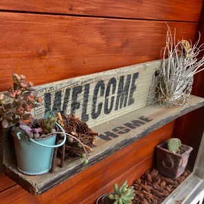 A wooden bench with a 'WELCOME' sign, decorated with succulents, a pine cone, and a cactus in a wire basket. - Tsubame-ya - Hostel (Kyoto)