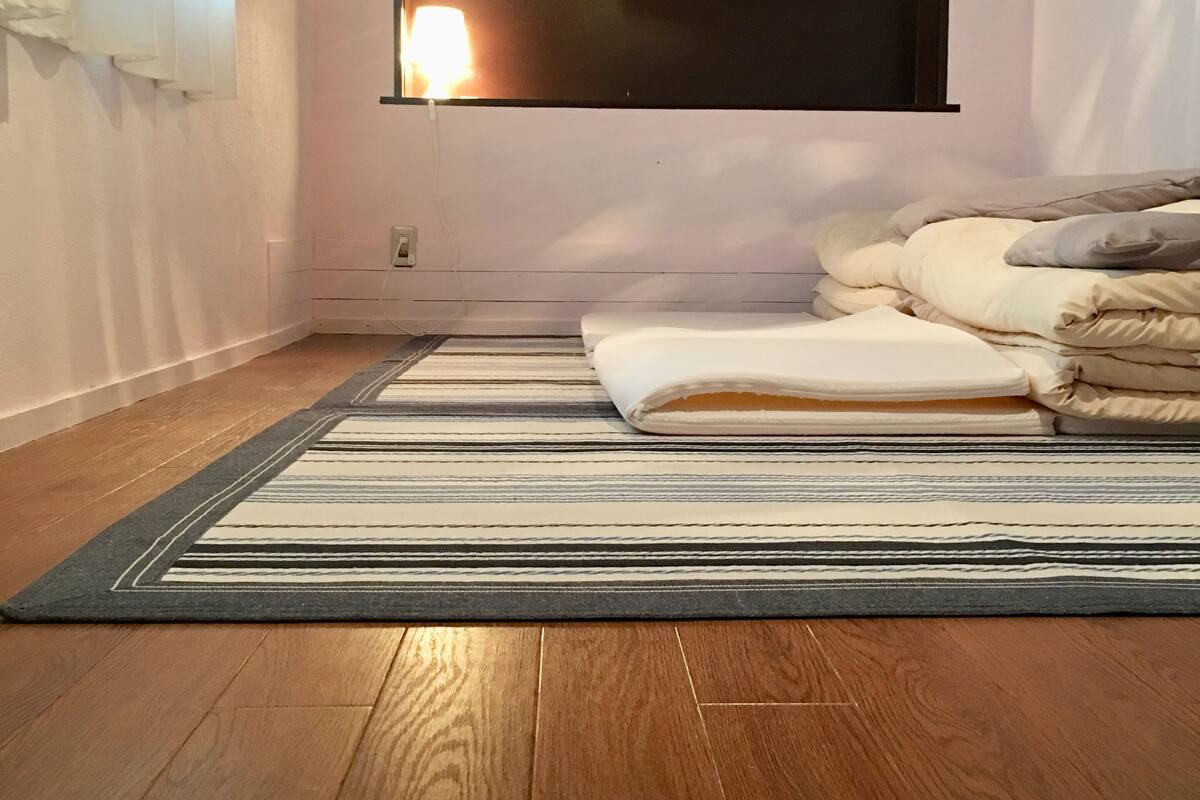 A bedroom with a bed, a window, an air conditioner, and a striped rug.