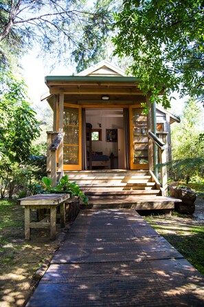 A wooden cabin with a porch, a staircase, and a small table with plants. - Hush Boutique Accommodation (Coromandel)