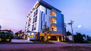 A modern hotel with a prominent 'B' logo, multiple floors, and a well-lit entrance. - B Boutique Residence (Surat Thani)