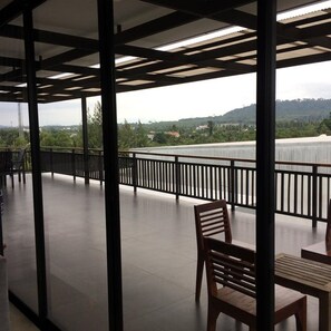 A spacious balcony with a view of a hilly landscape, featuring a wooden chair and a table. - B Boutique Residence (Surat Thani)