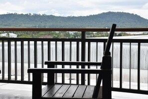 A wooden bench on a balcony with a view of a hill and buildings in the distance. - B Boutique Residence (Surat Thani)
