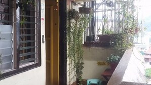 A small room with a bed, a window, and a door. There are plants and a sign on the wall. - CVNB Bed & Bath - Hostel (Baguio)