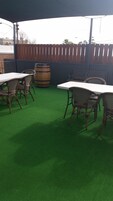 Un área de patio al aire libre con mesas y sillas, un barril de madera y piso de césped artificial verde.