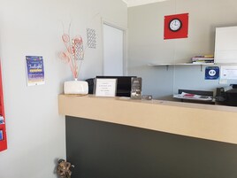 Zona de recepción de un hotel, con mostrador de recepción, un reloj, un certificado enmarcado y un cartel en la pared.