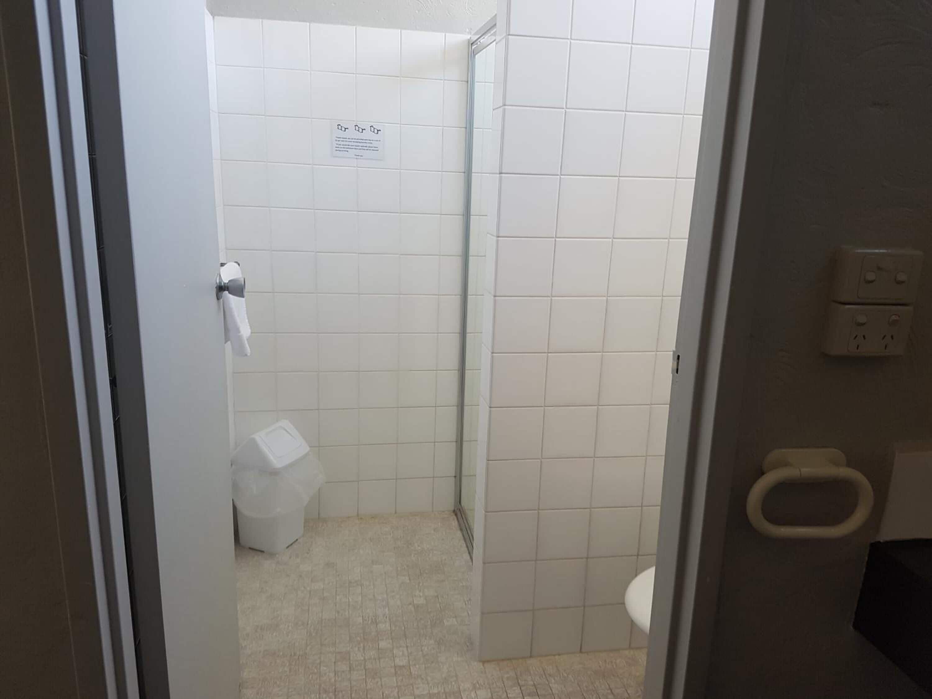 A small, tiled bathroom with a toilet, a trash bin, and a shower area.