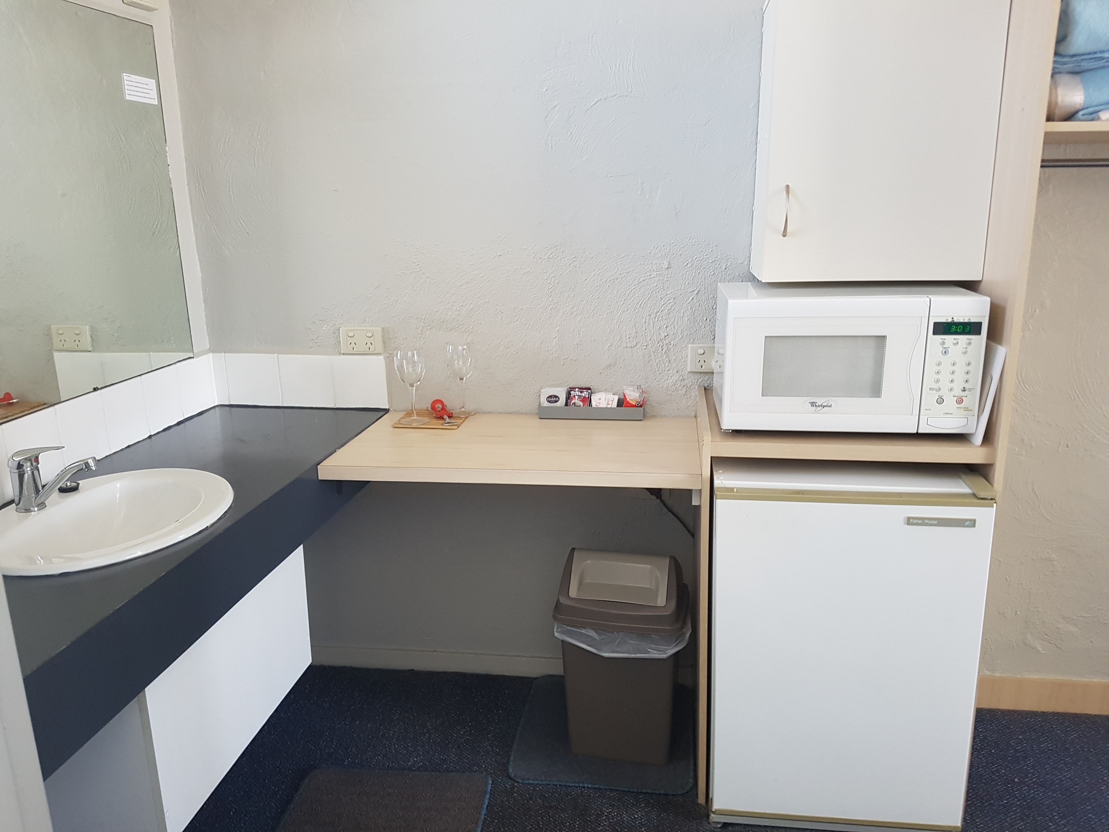 A compact kitchenette with a white sink, a microwave, and a small trash bin.
