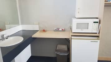 A compact kitchenette with a white sink, a microwave, and a small trash bin.