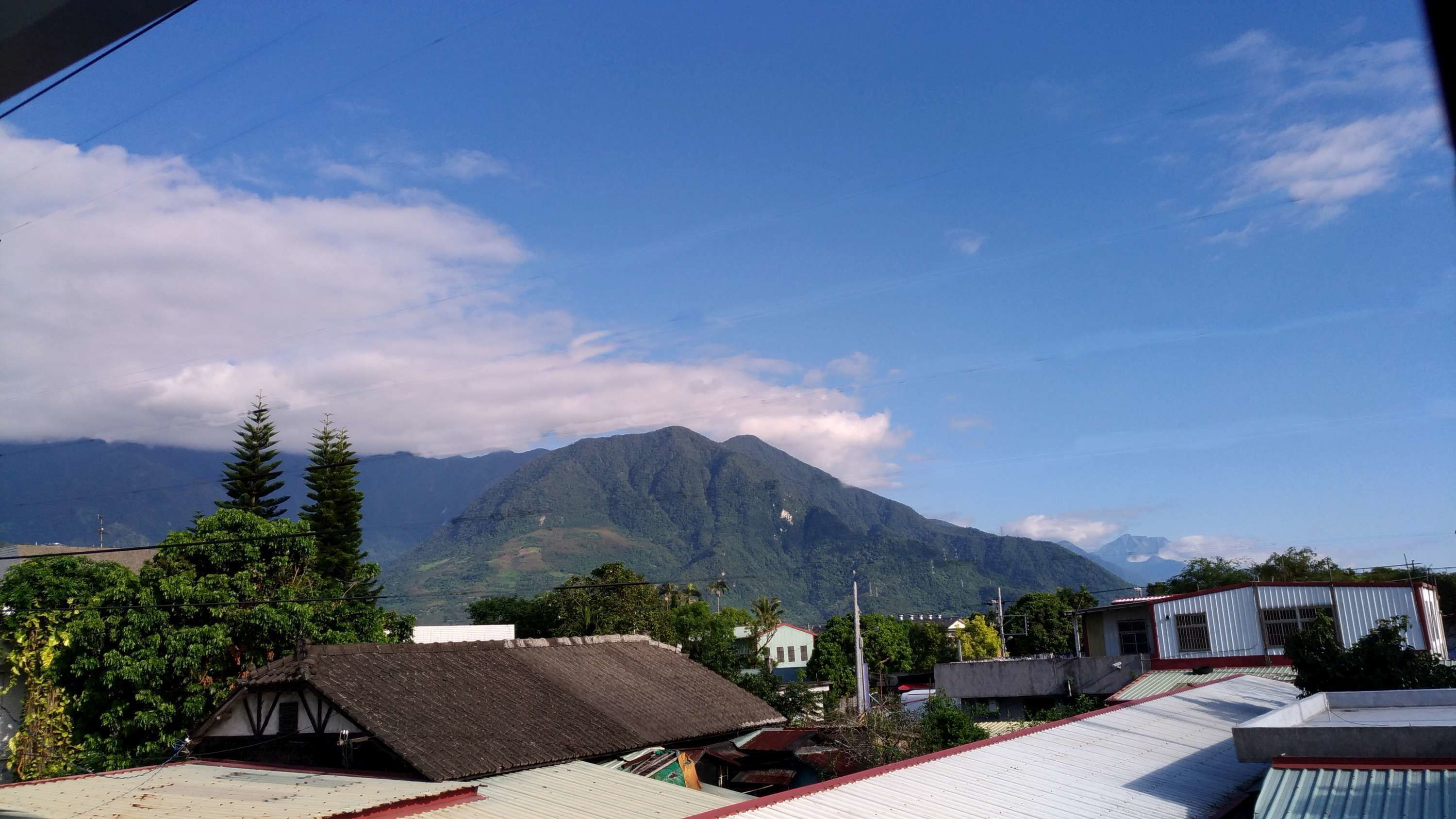 A mountain range with a clear sky. There are buildings with red roofs in the foreground.
