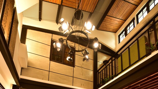 Un intérieur aux hauts plafonds, agrémenté d’un lustre central, de poutres en bois et d’un balcon doté d’une balustrade.