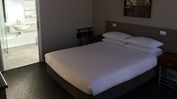 Ein Hotelzimmer mit einem großen Bett, einem Nachttisch, einem Schreibtisch, einem Bild an der Wand und einem sichtbaren Badezimmer durch eine offene Tür.