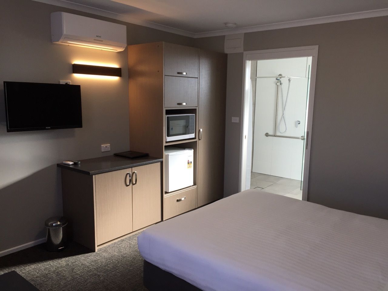 A hotel room with a bed, a kitchenette with a microwave, a TV, and a shower area.